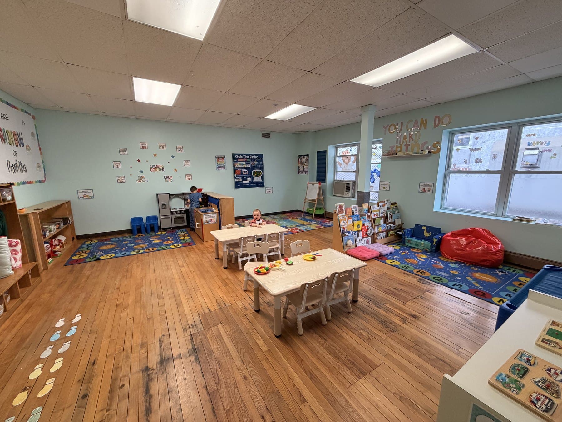 A full classroom: alphabet rugs, a play kitchen, the reading rack and the Circle Time board, with the words You can do hard things painted on the far wall.